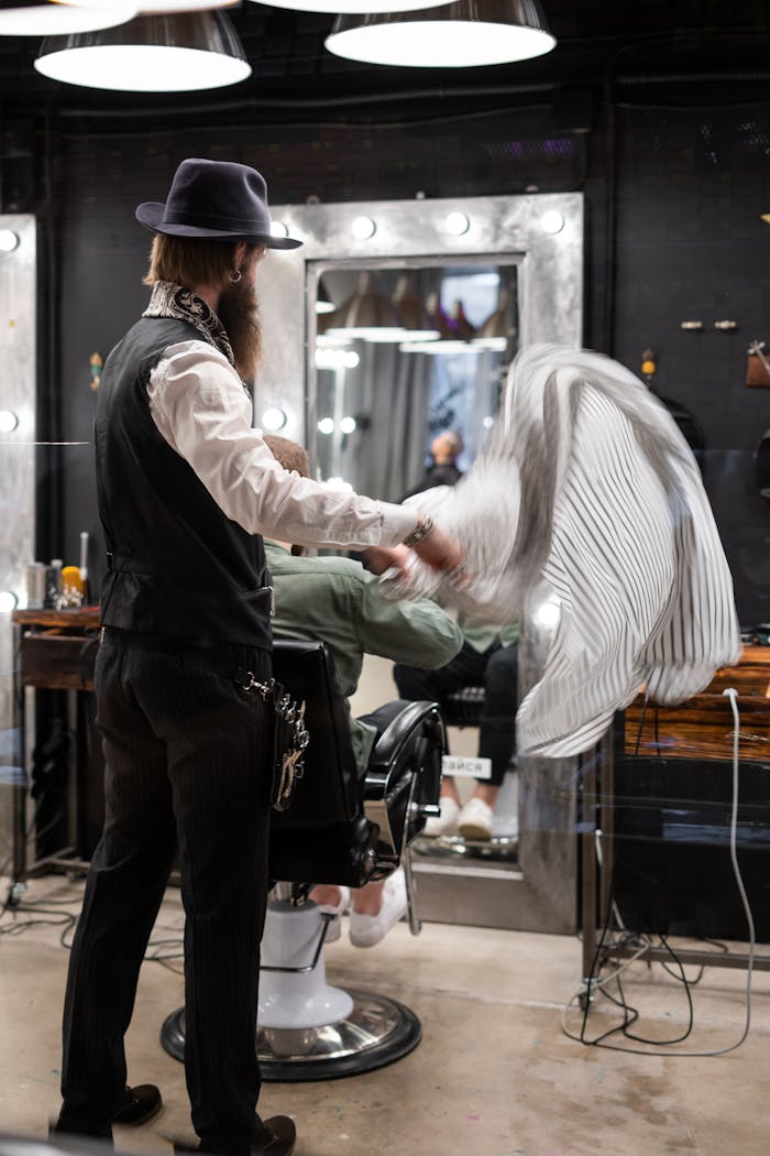A stylish bearded barber in casual attire at a trendy barbershop prepares for a haircut.